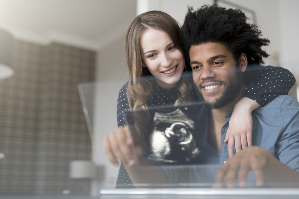Smiling couple looking at ultra sound picture of baby on futuristic screen